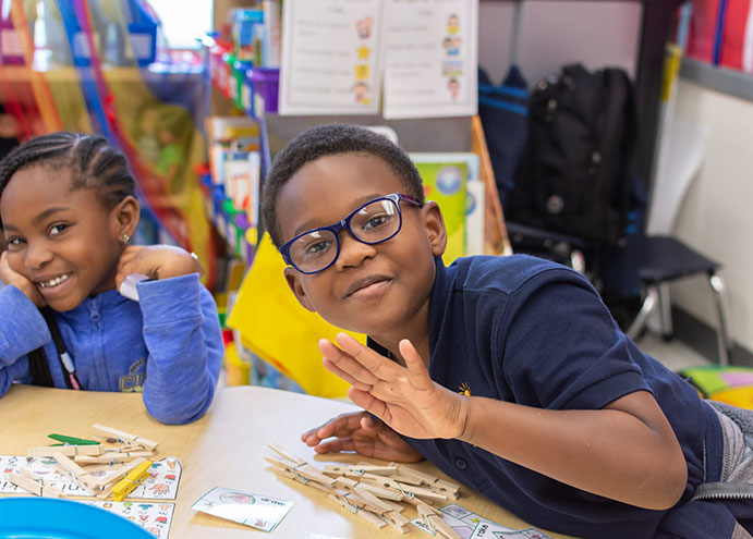 children in classroom smiling and waving