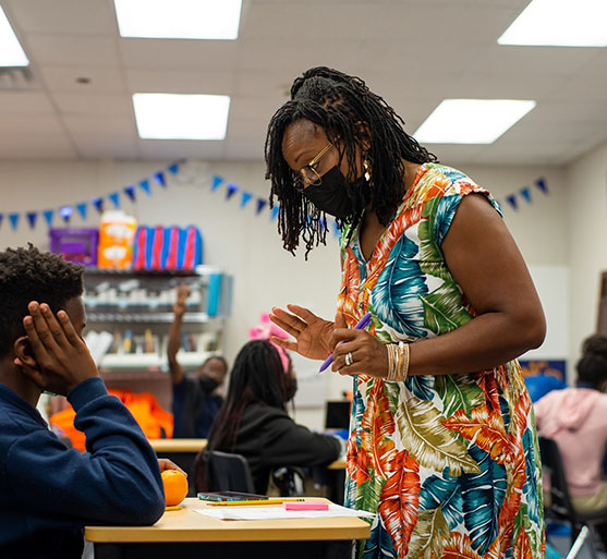 teacher in classroom explaining to sitting student