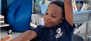 young student raising hand in classroom and smiling